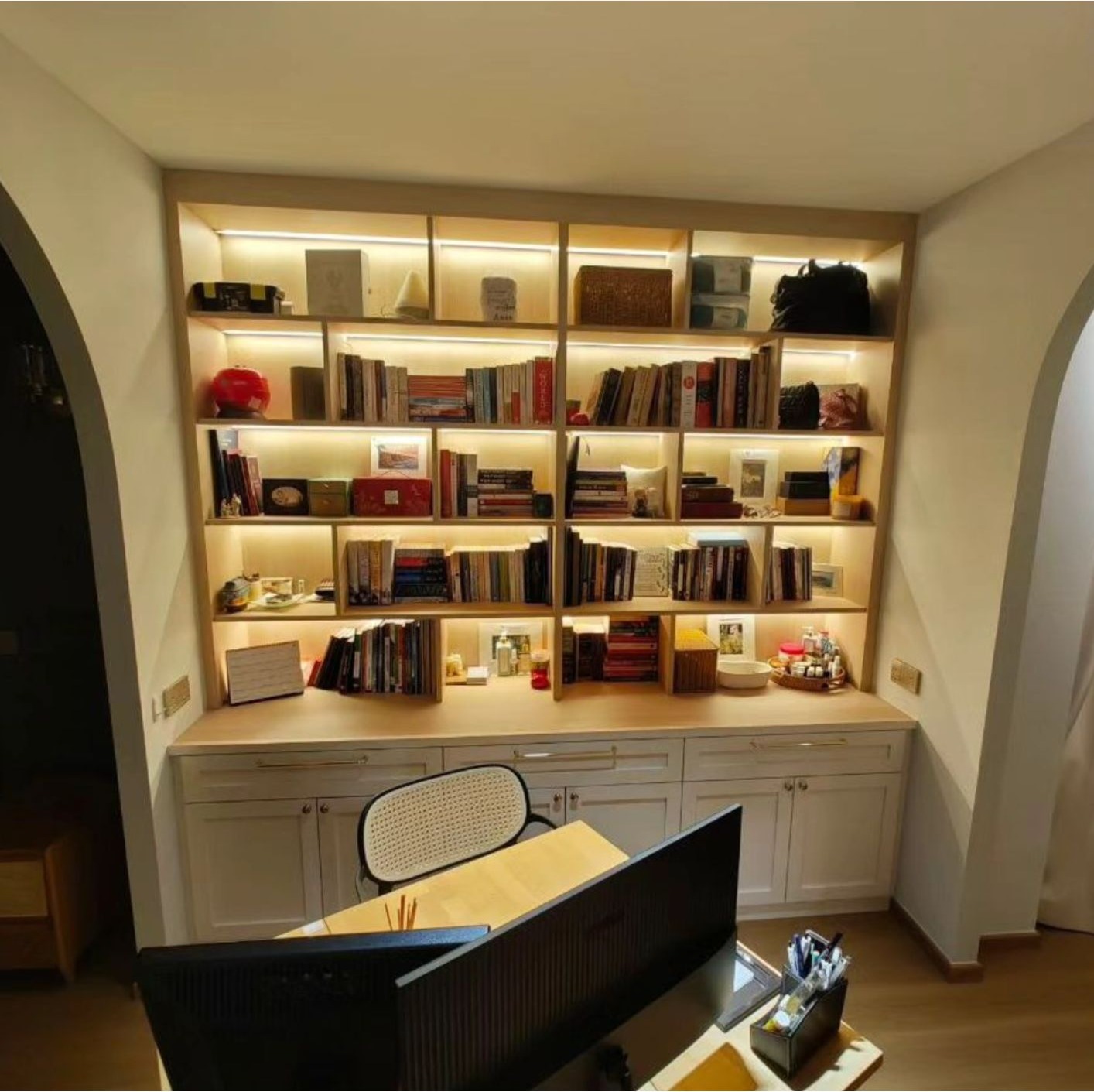Study room with full-wall bookshelf, LED-lit compartments, timber desk and rattan chair