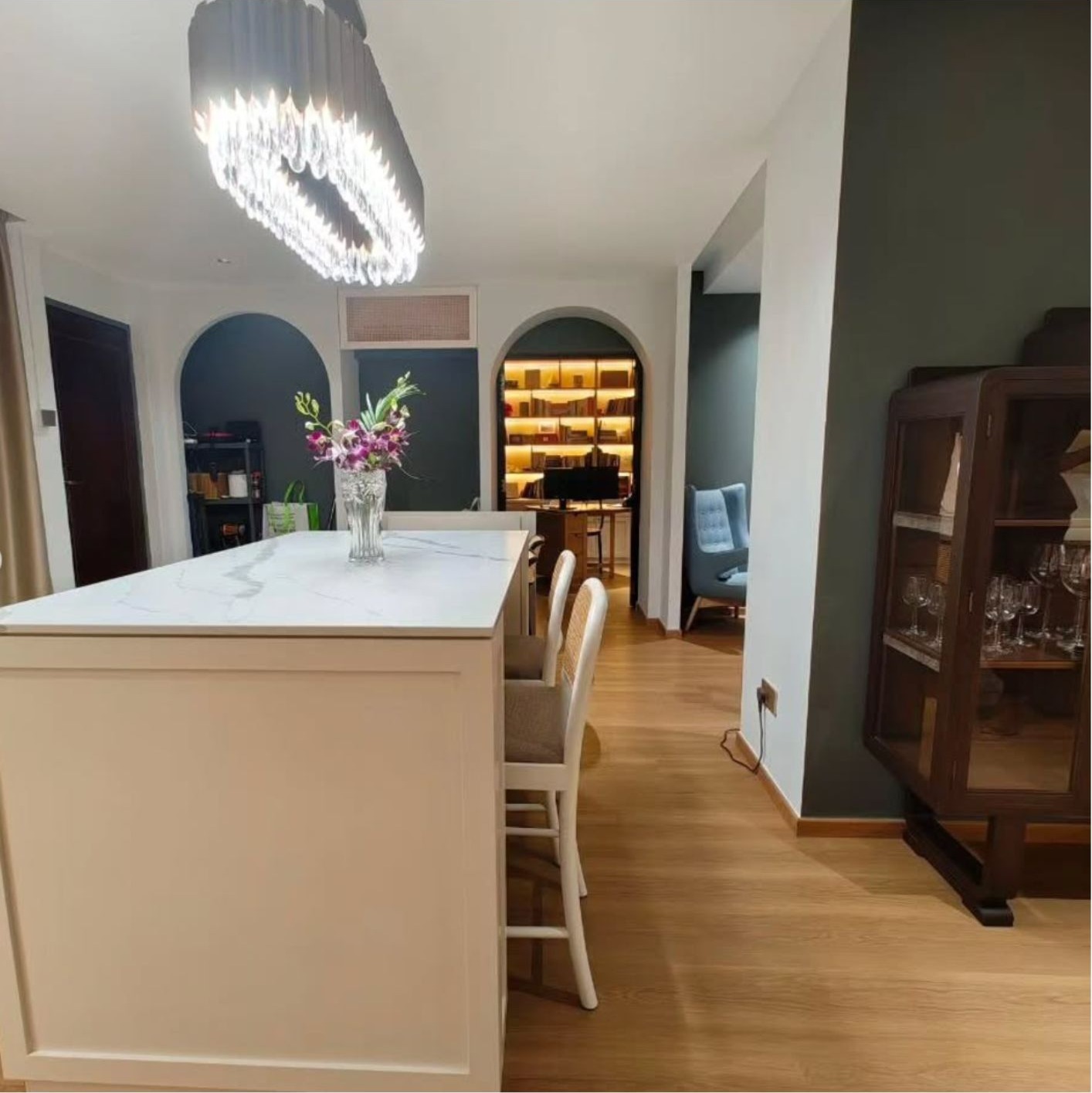 Dining area with white marble island, crystal chandelier, arched doorways and vintage glass cabinet