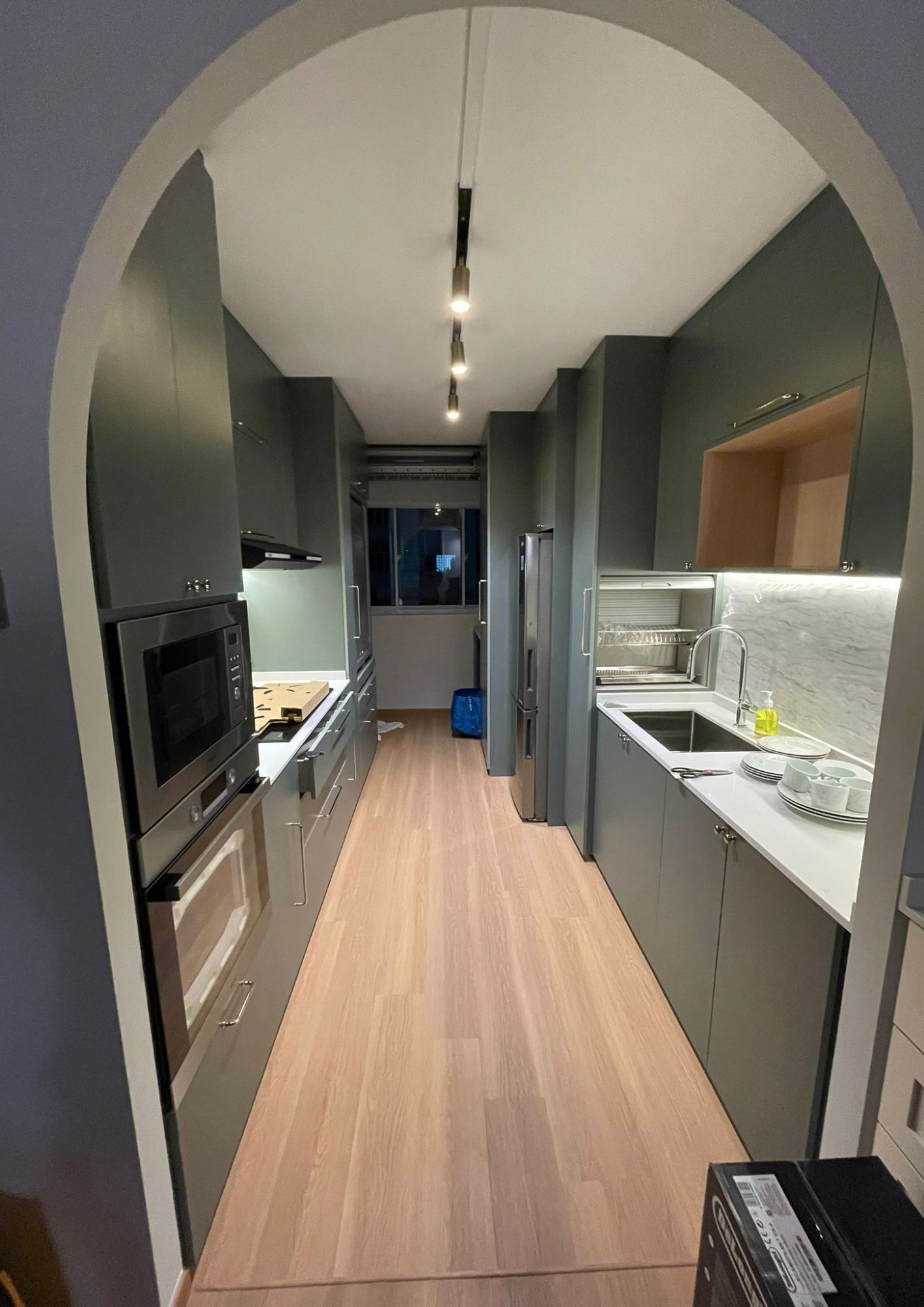 Kitchen with sage green cabinetry through arched doorway, light wood floor and pendant lights