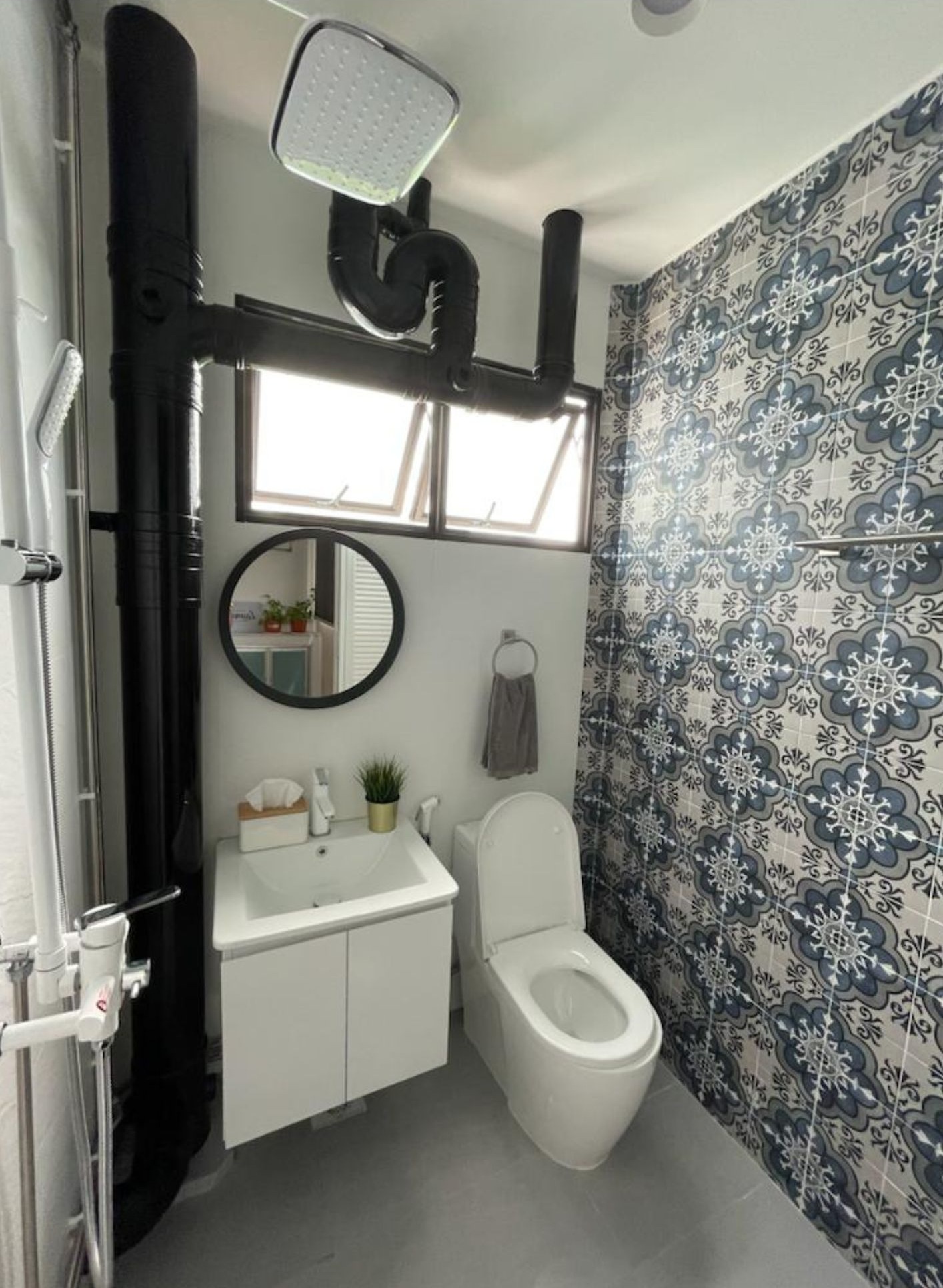 Common bathroom with blue Portuguese patterned tile feature wall, round black mirror and white vanity