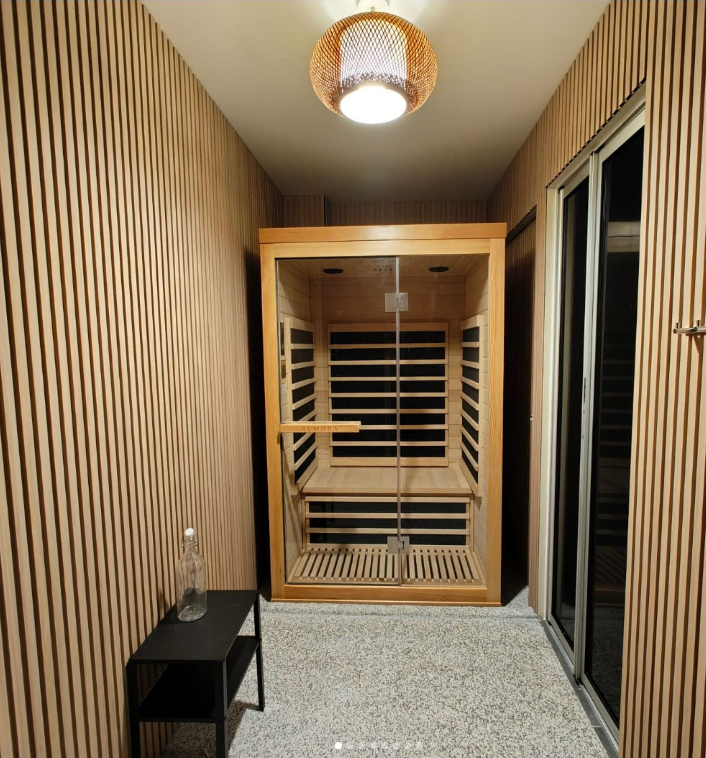 Infrared sauna room with timber slat walls, woven pendant light and glass door cabin
