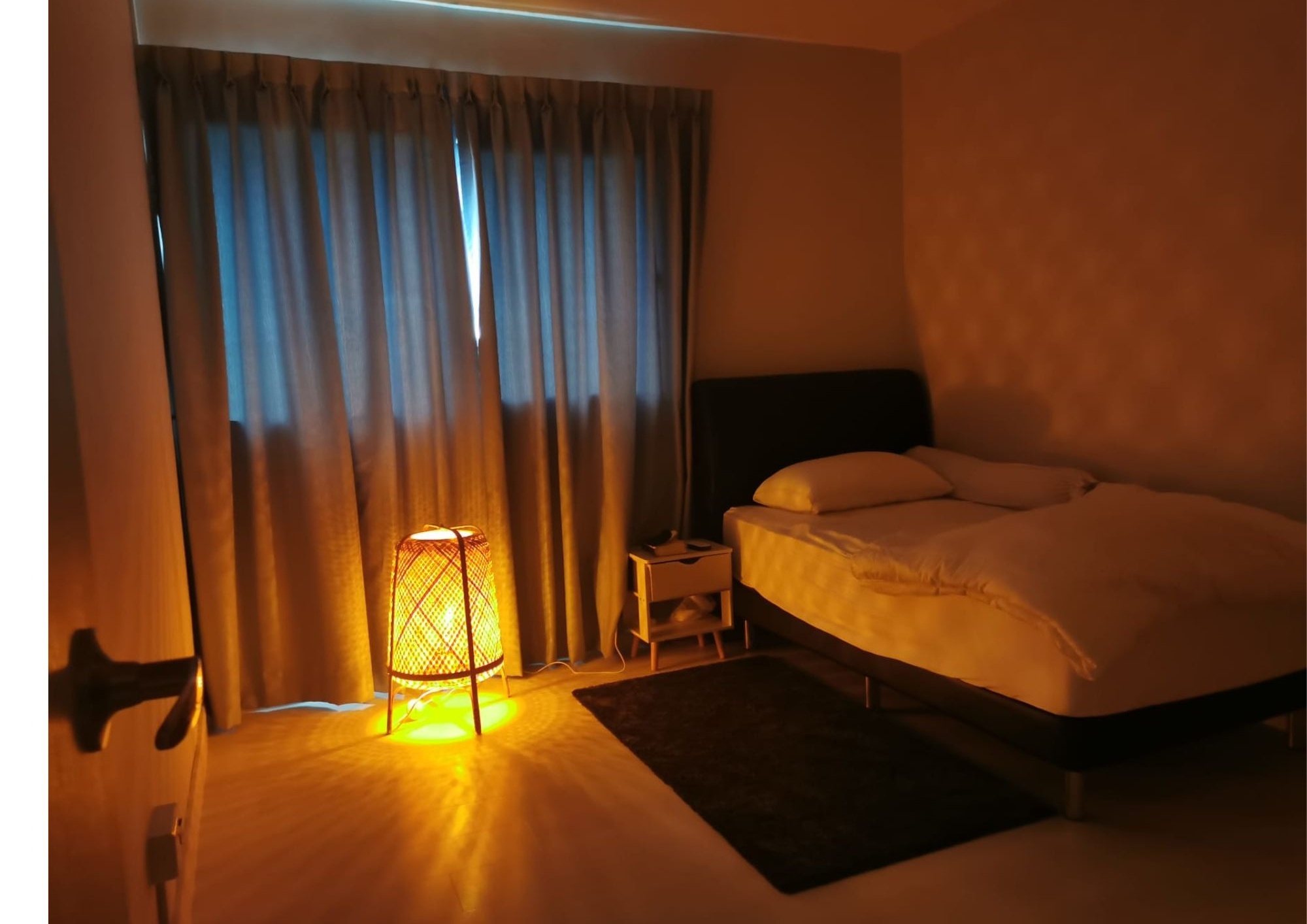 Common bedroom with warm rattan floor lamp, dark headboard and ambient lighting